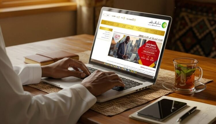 A person types on a laptop showing the Bank of Khartoum internet banking page, with a glass of tea and a phone on the desk.