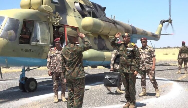 Army officers salute beside a military helicopter on an airstrip as Abdel Fattah al-Burhan arrives.