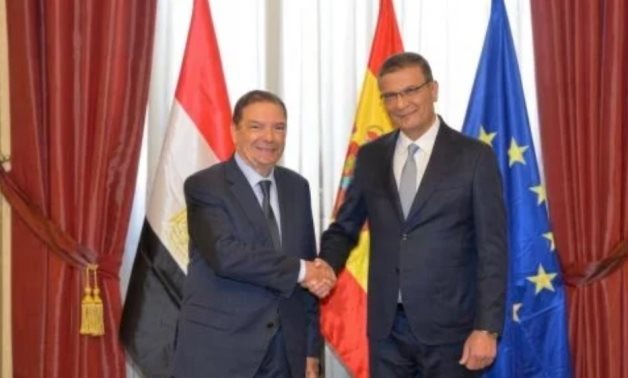 Two men in suits shake hands in front of Egyptian, Spanish and European Union flags.