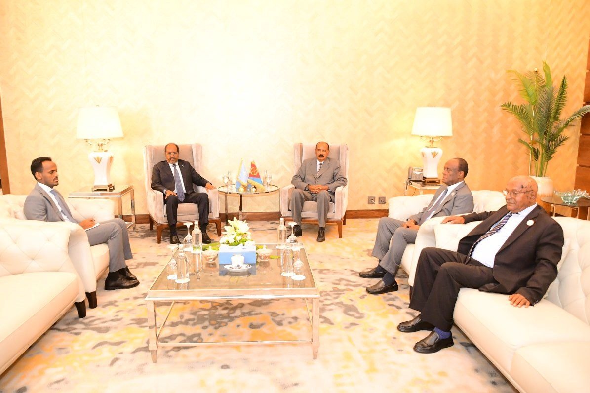 Two presidents sit in armchairs with small national flags between them while aides sit on sofas.