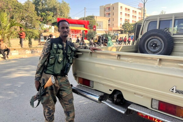 A soldier in camouflage stands beside a pickup truck on a town street.
