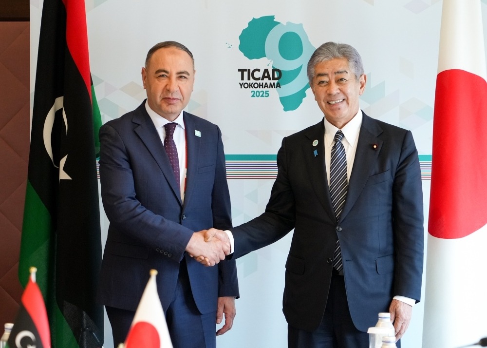 Two foreign ministers shake hands in front of a TICAD 9 Yokohama 2025 backdrop with Libyan and Japanese flags.