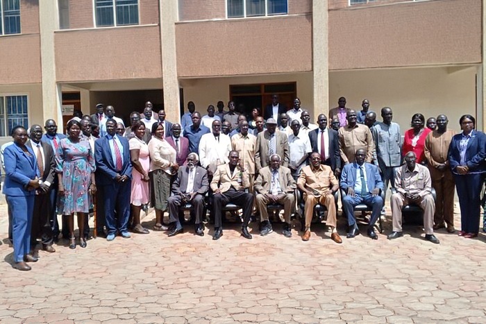 Church leaders and delegates pose for a group photo in a paved courtyard outside a building.