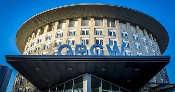 The curved facade of a building carrying the letters OPCW against a blue sky.