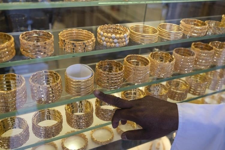 A hand points to shelves of gold bracelets in a jewellery shop display.